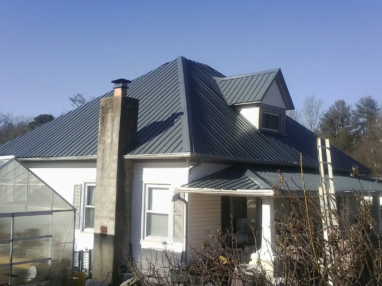 Dark blue standing seam metal roof on a white farmhouse with dormer — Slate & Tile Roof Repair by Roofing Brothers in Hagaman