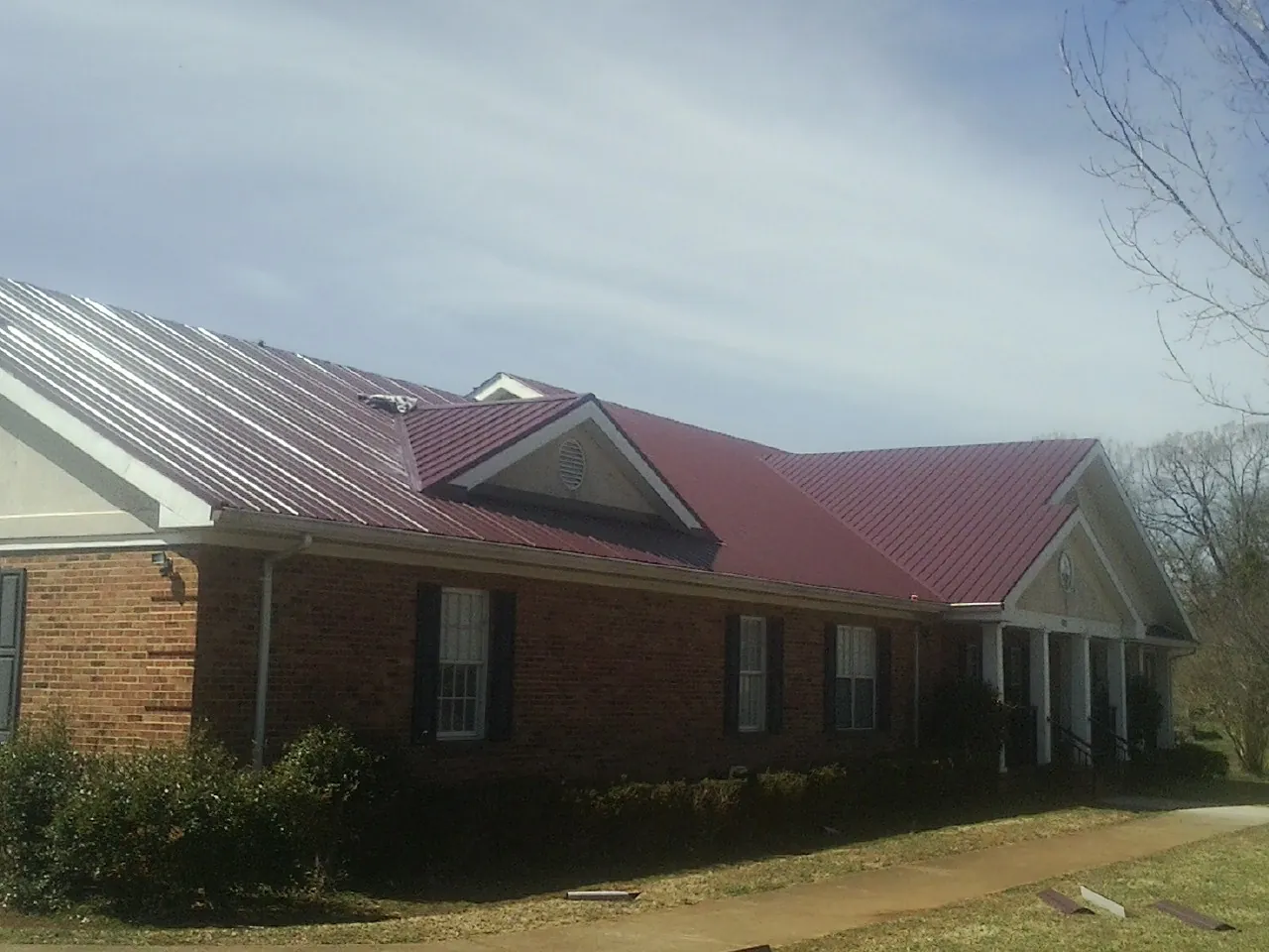 Red metal roof with gabled entries on a long brick building, from a Hail Damage Roof Repair job in Hagaman