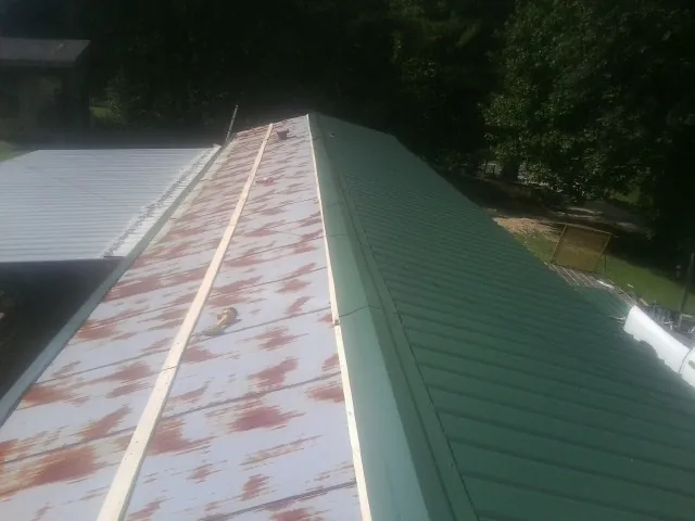 Old rusted panels beside newly installed green metal roofing — Wind Damage Roof Repair by Roofing Brothers in Hagaman