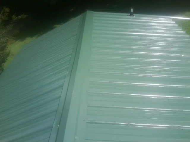 New green metal panels meeting at the ridge of a roof — Flat Roof Repair work by our crew in Hagaman