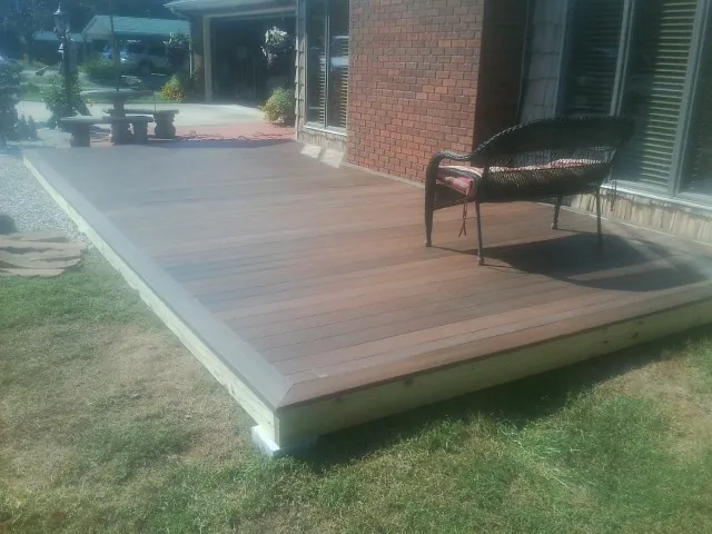 New wood deck and wicker chair beside a brick house in Hagaman