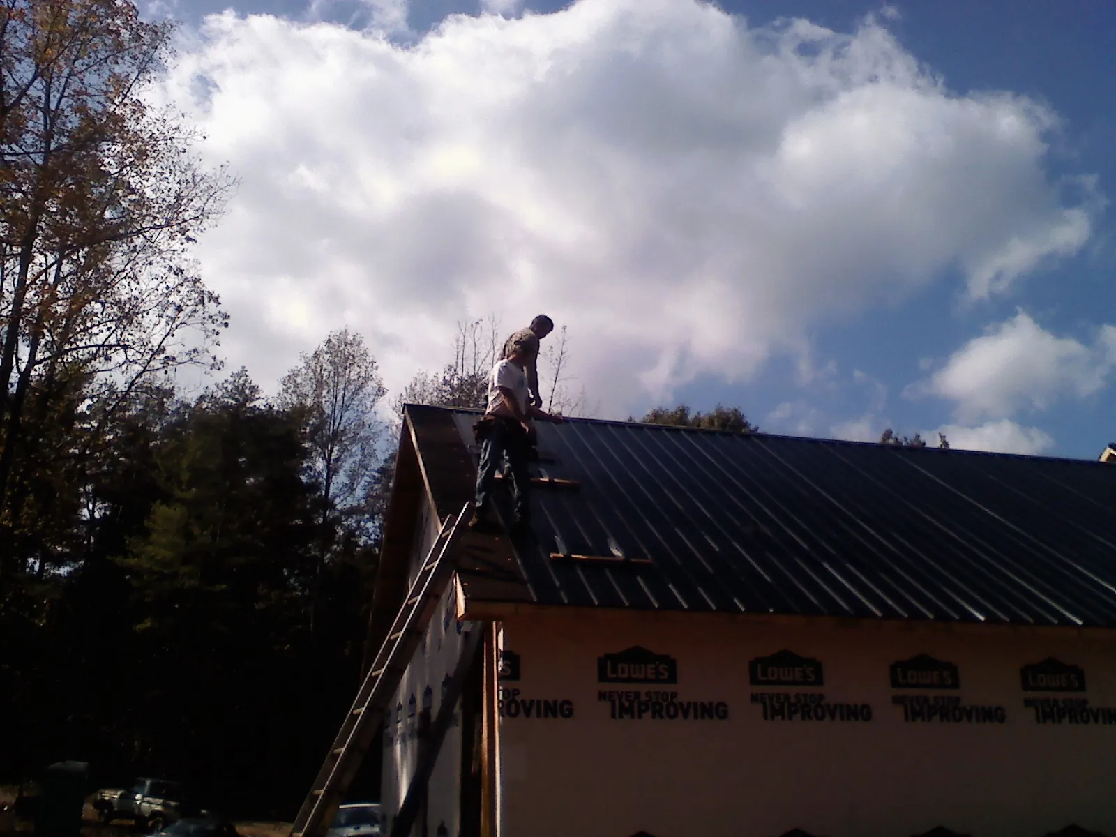 Roofer fastening dark metal panels high against a cloudy sky, from a Roof Inspection job in Hagaman