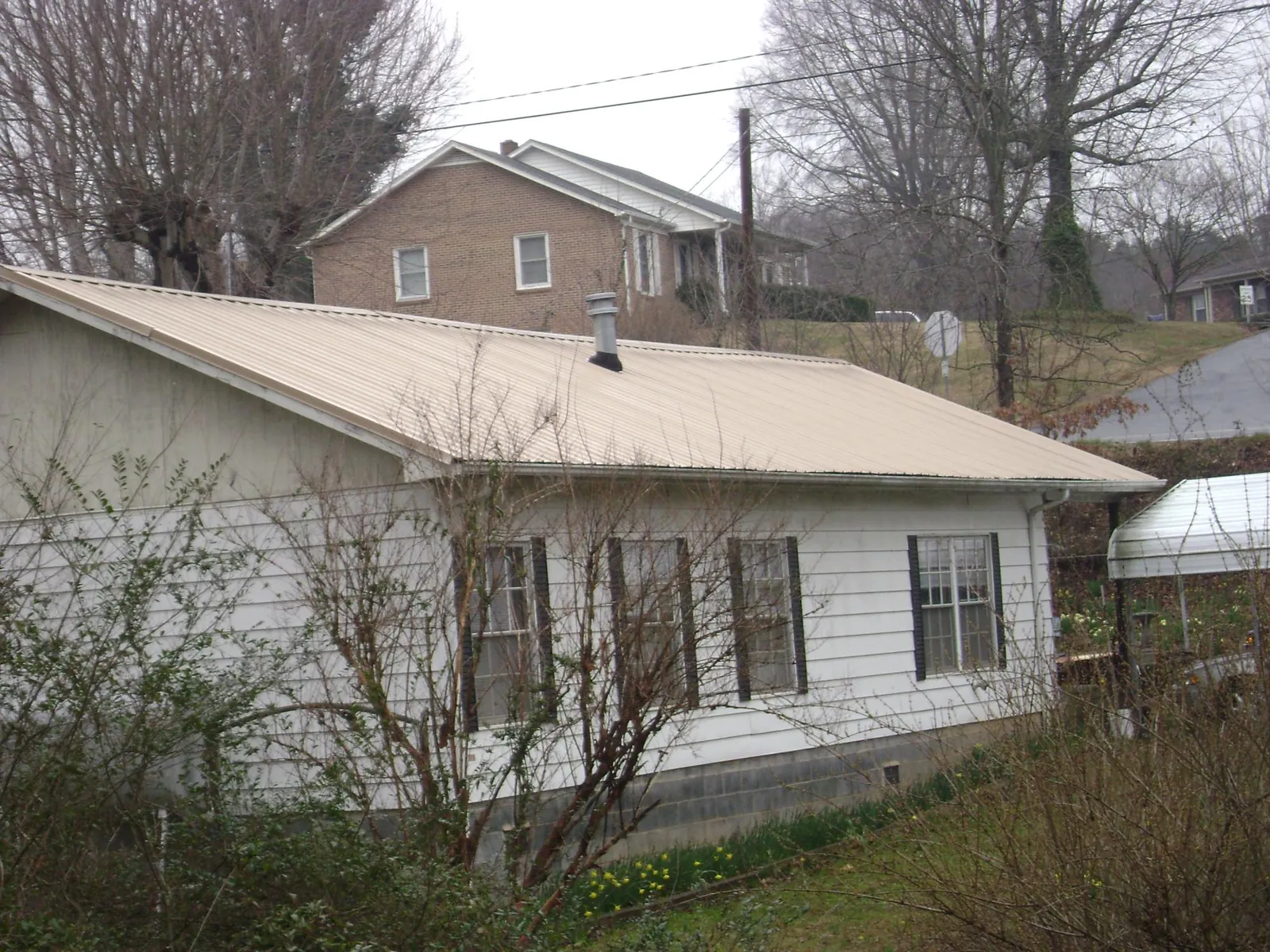 Tan metal roof on a white sided house set into a hillside — Commercial Roofing by Roofing Brothers in Hagaman