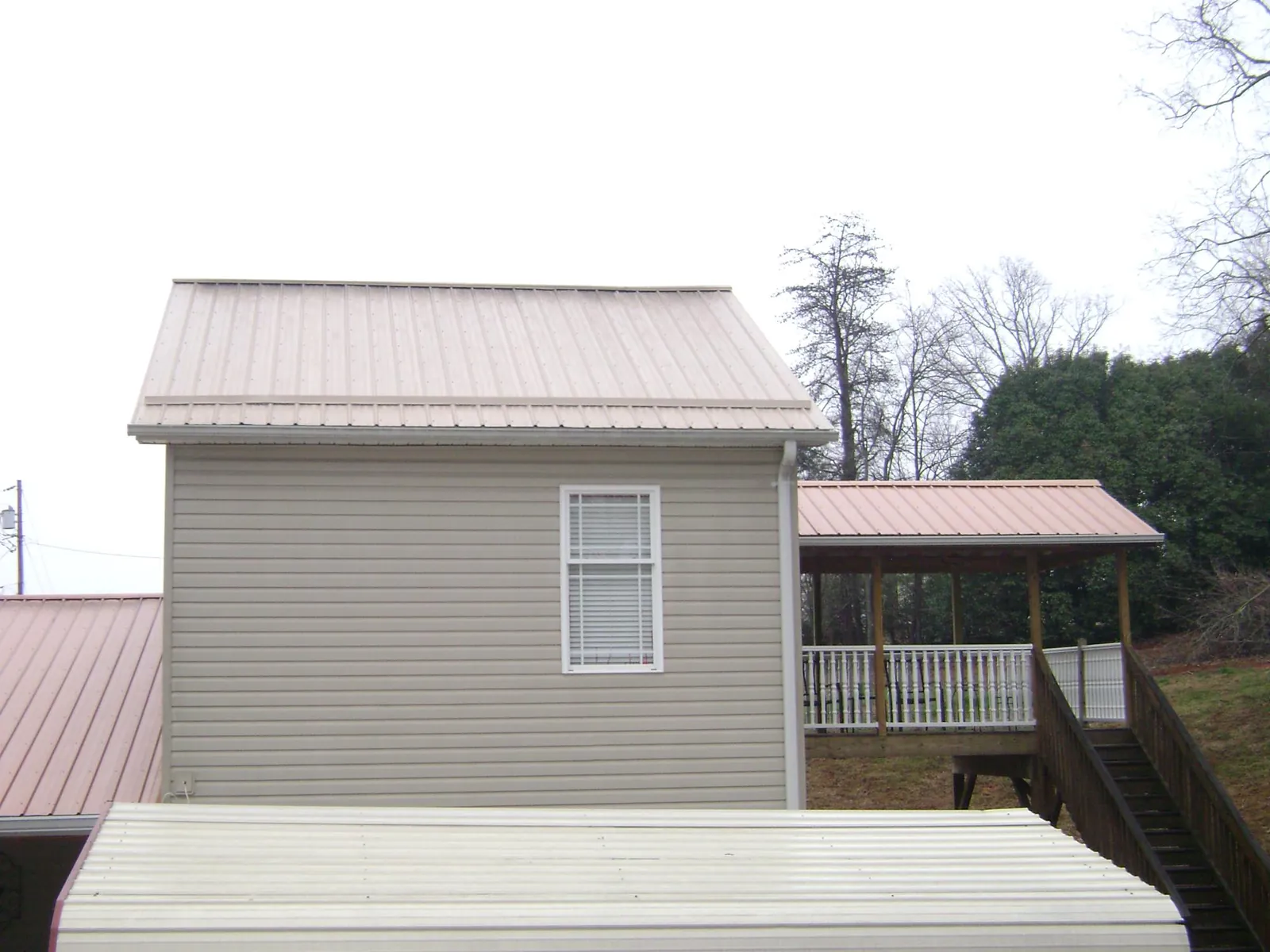 Tan metal roofs on a two story addition and attached porch, from a Roof Replacement job in Hagaman